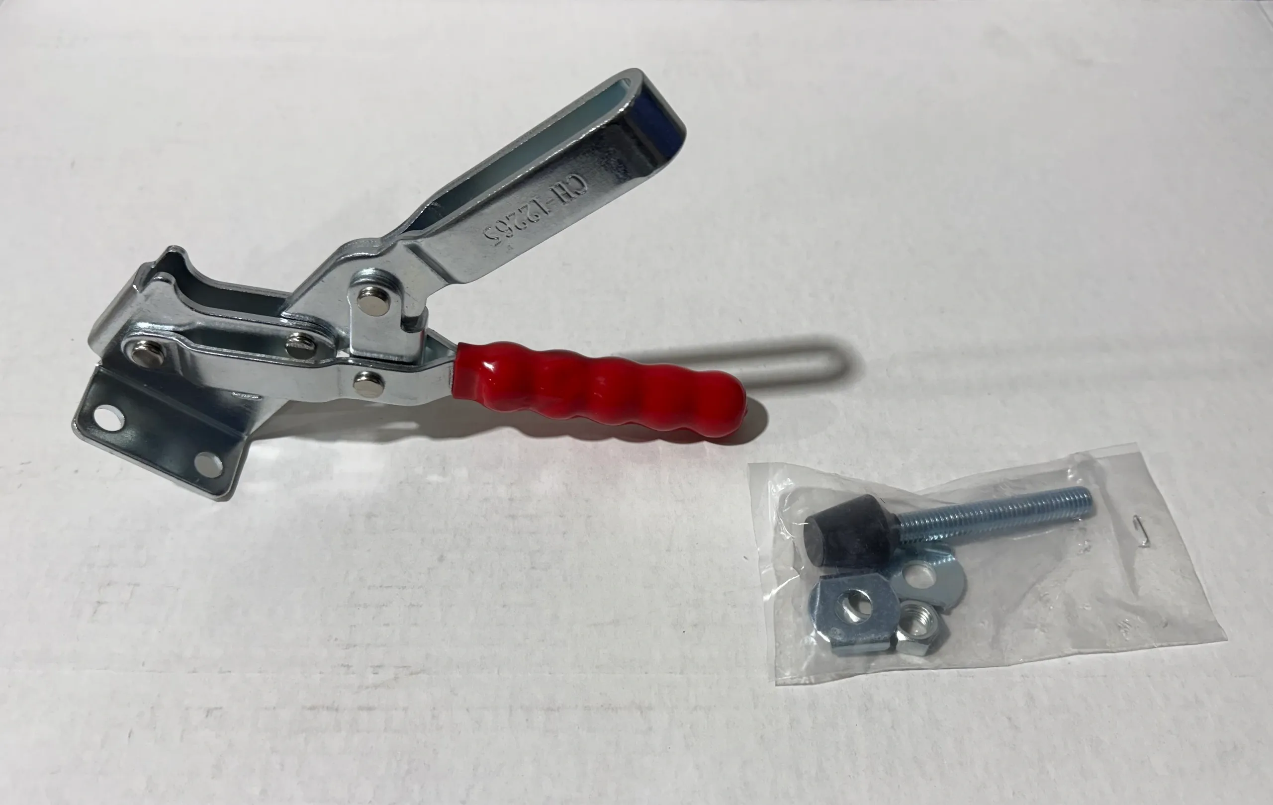 A metal clamp with a red handle and a small metal object in a plastic bag.