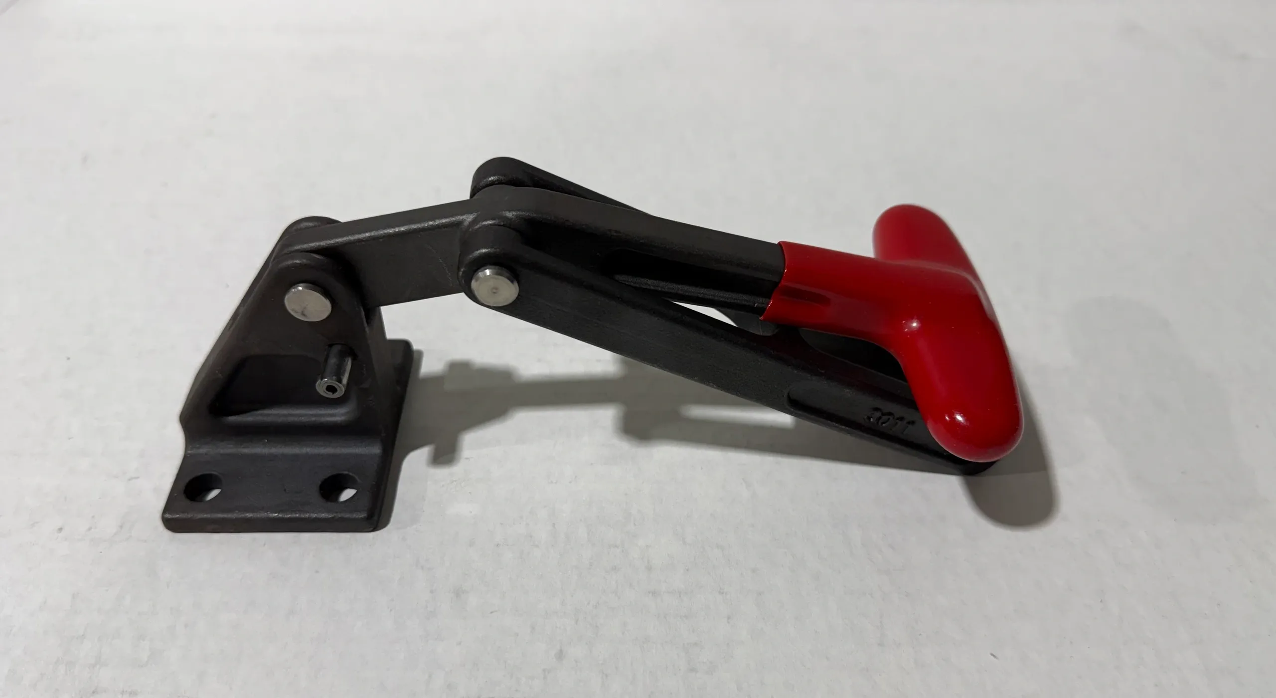 A black and red toggle clamp on a white surface.