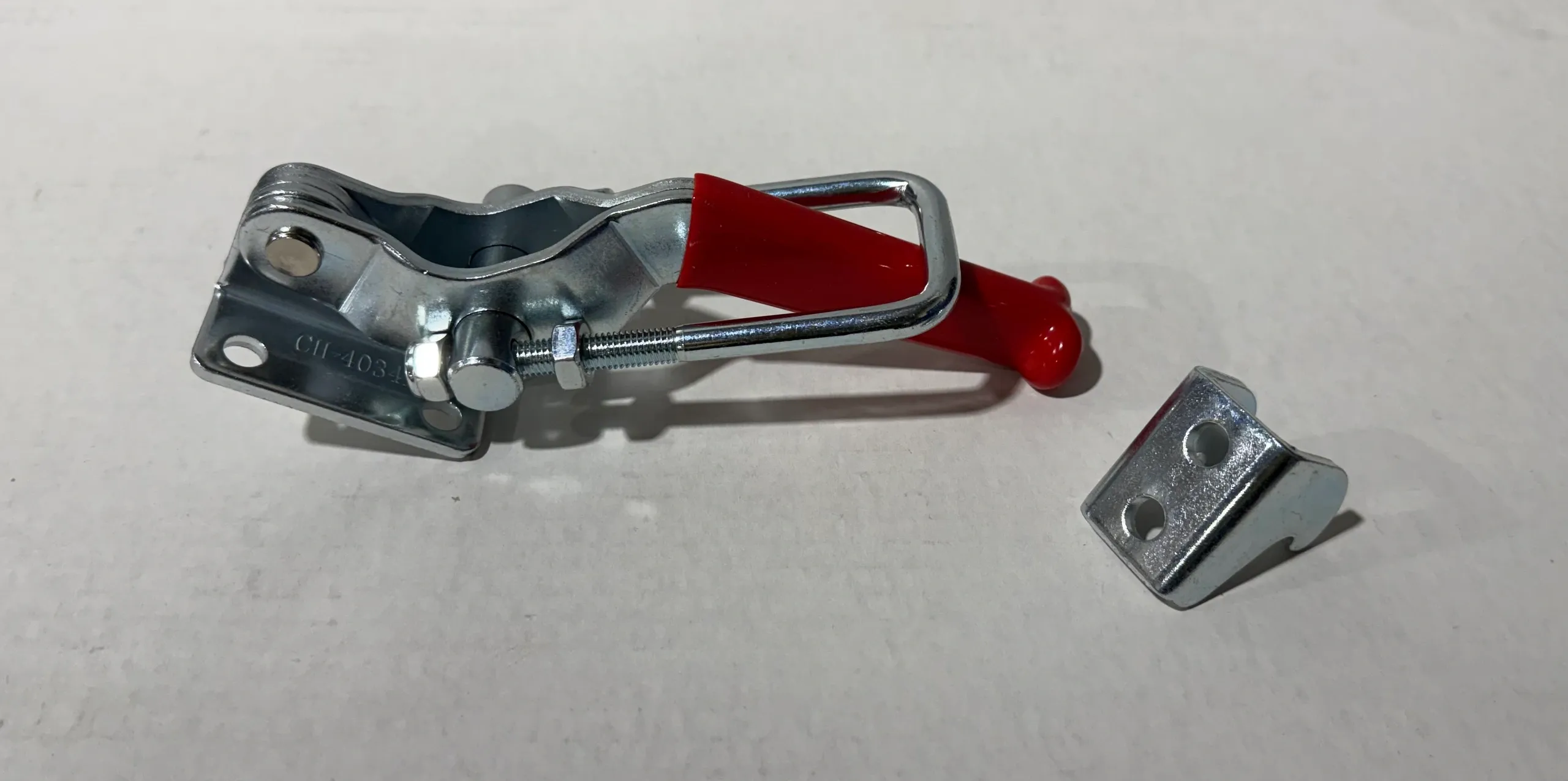 A metal toggle latch with a red handle and screws on a white background.