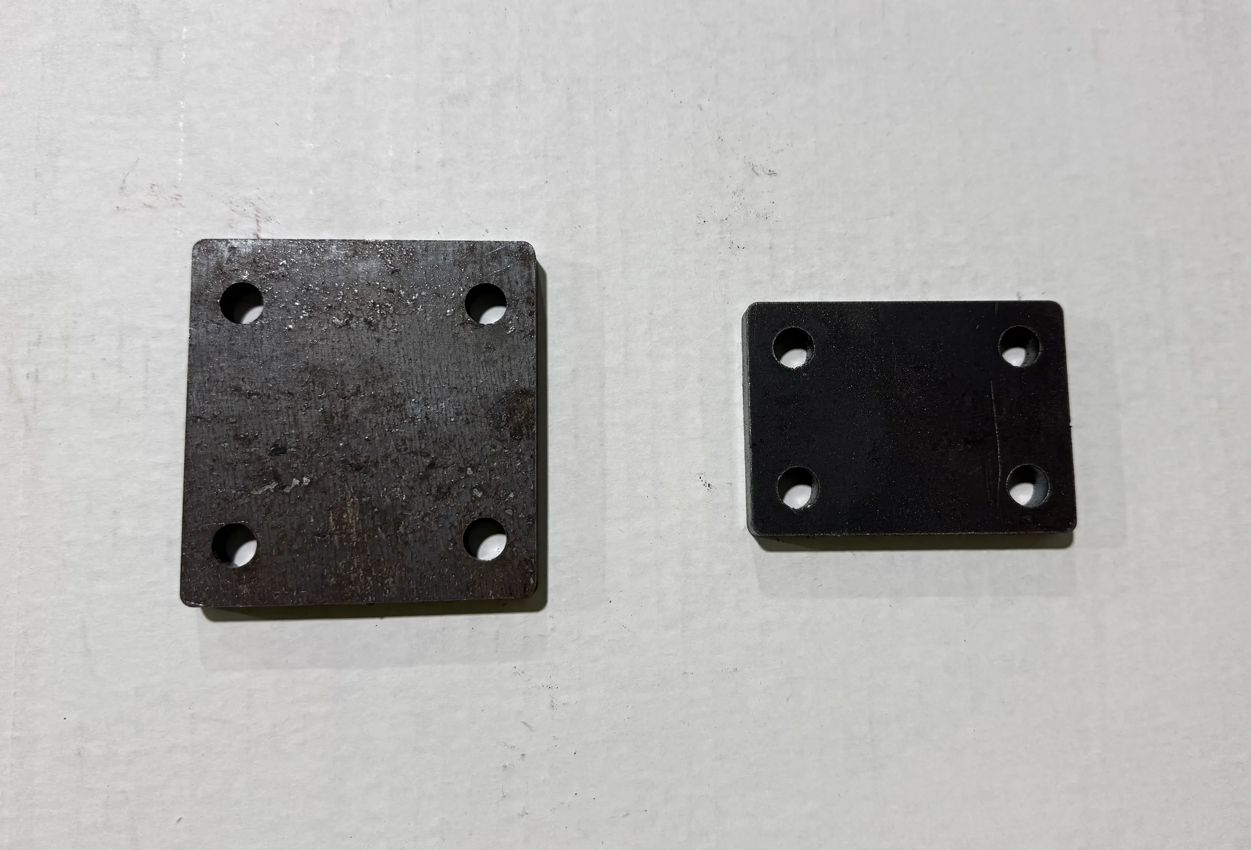 Two black metal plates with holes on a white surface.