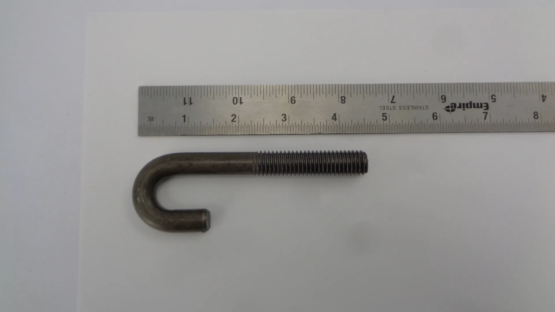 Metal J-bolt with a ruler for scale.