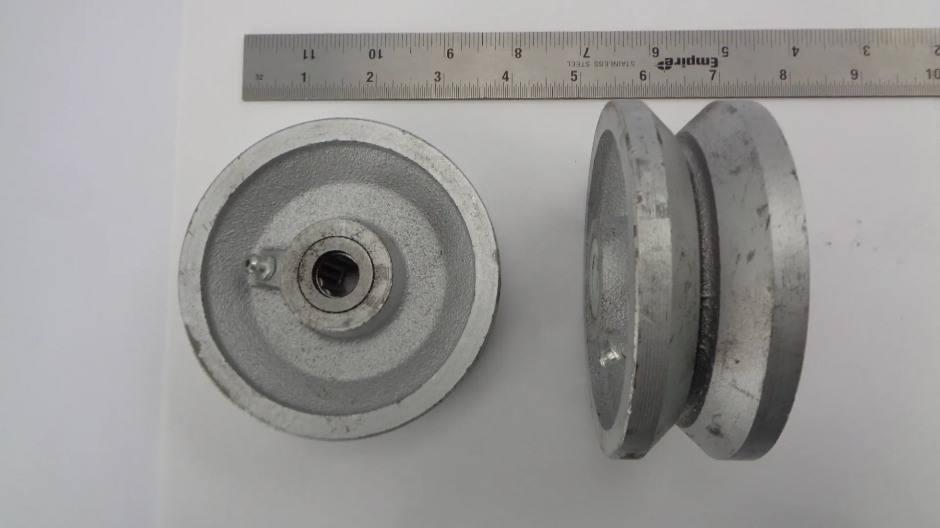 Two metal pulleys with a ruler for scale, showing precise engineering.