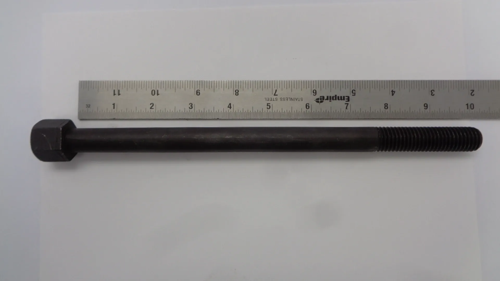 A metal rod placed next to a ruler on a white surface.