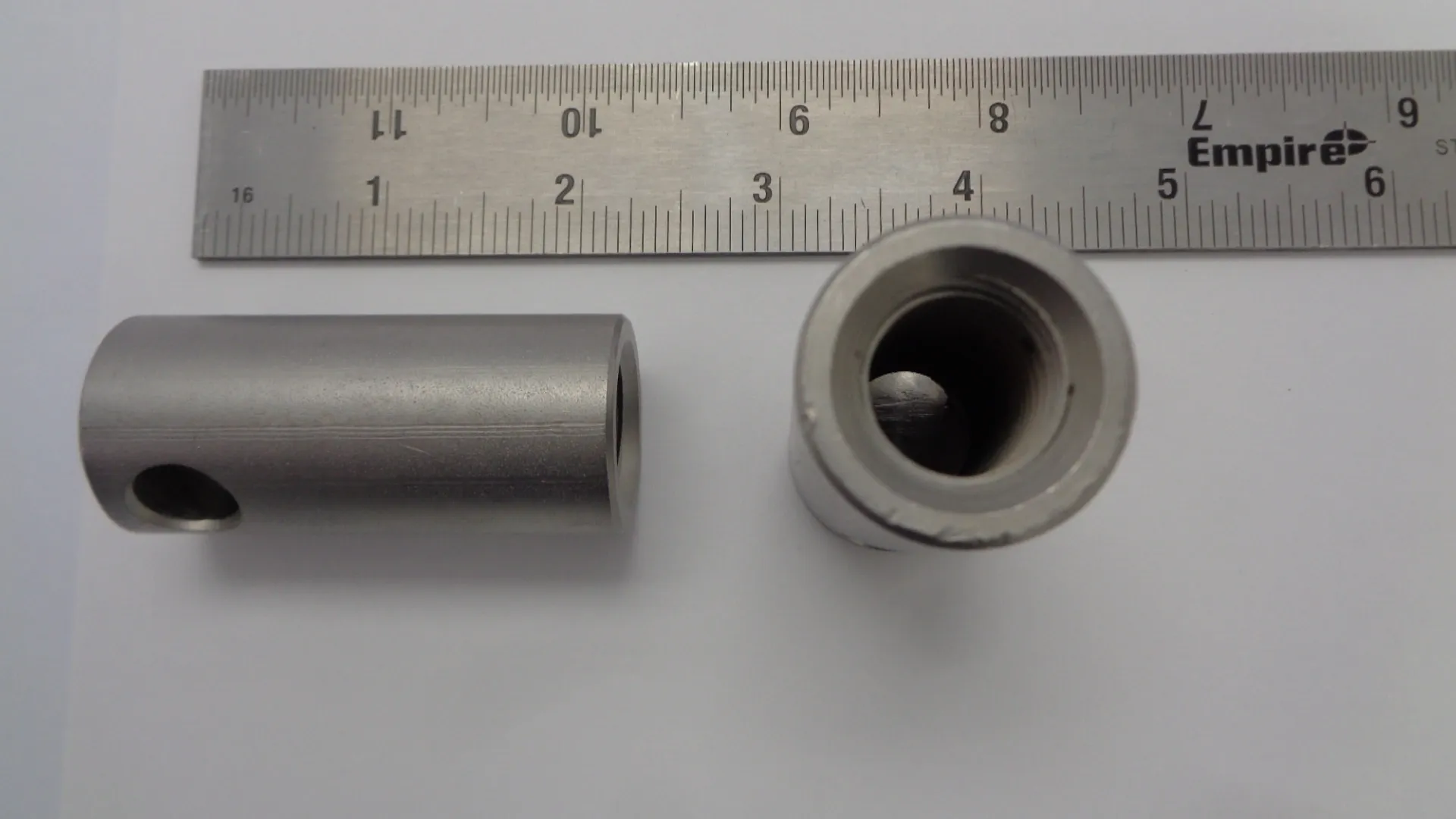 Two metallic cylindrical parts placed beside a ruler for size reference.