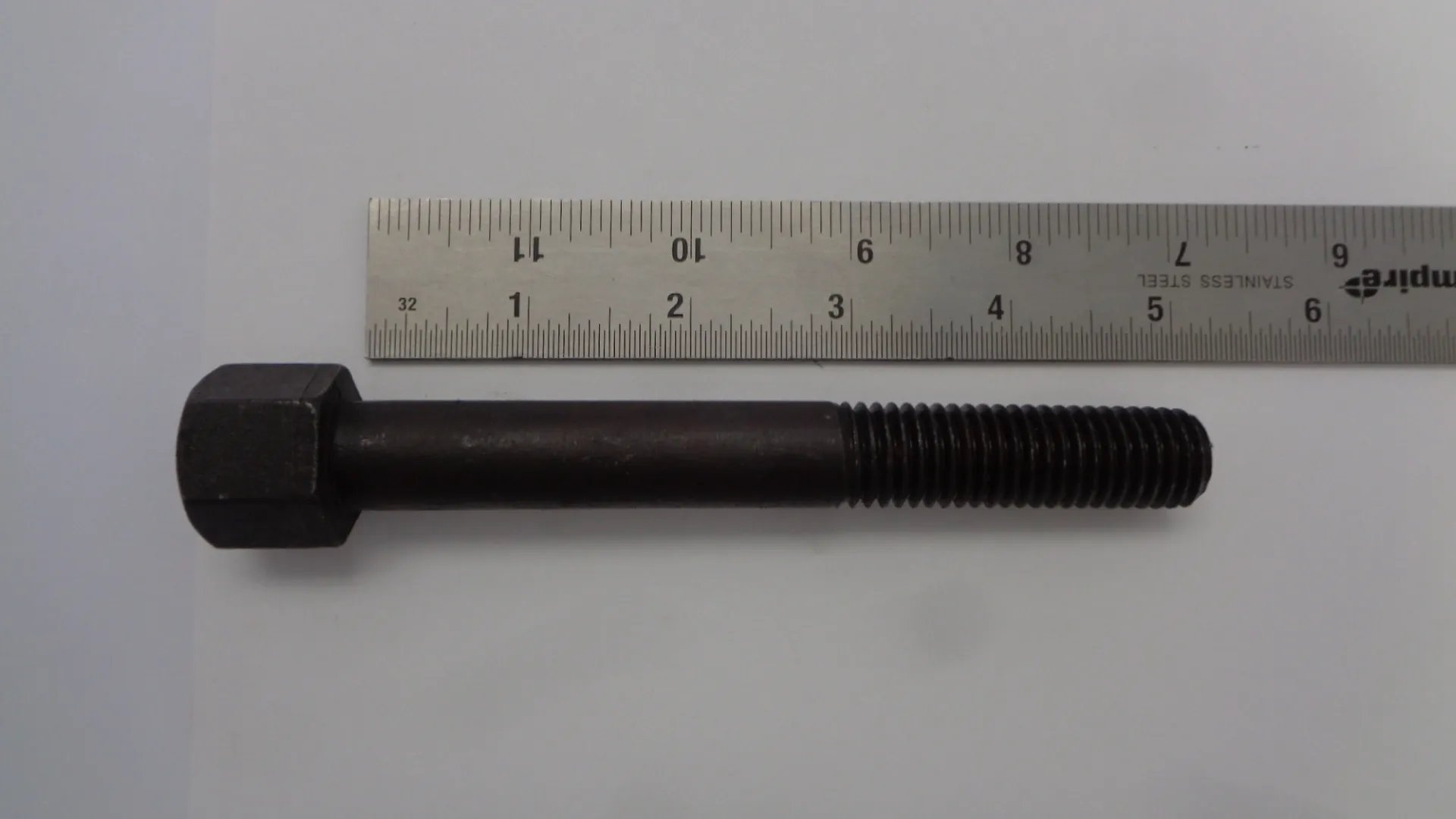 A black metal bolt with a ruler for size reference.