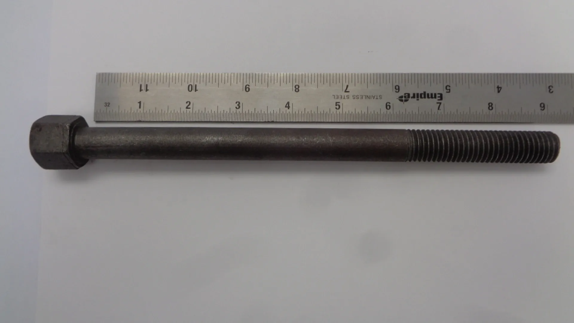 A metal bolt placed next to a ruler for size reference.
