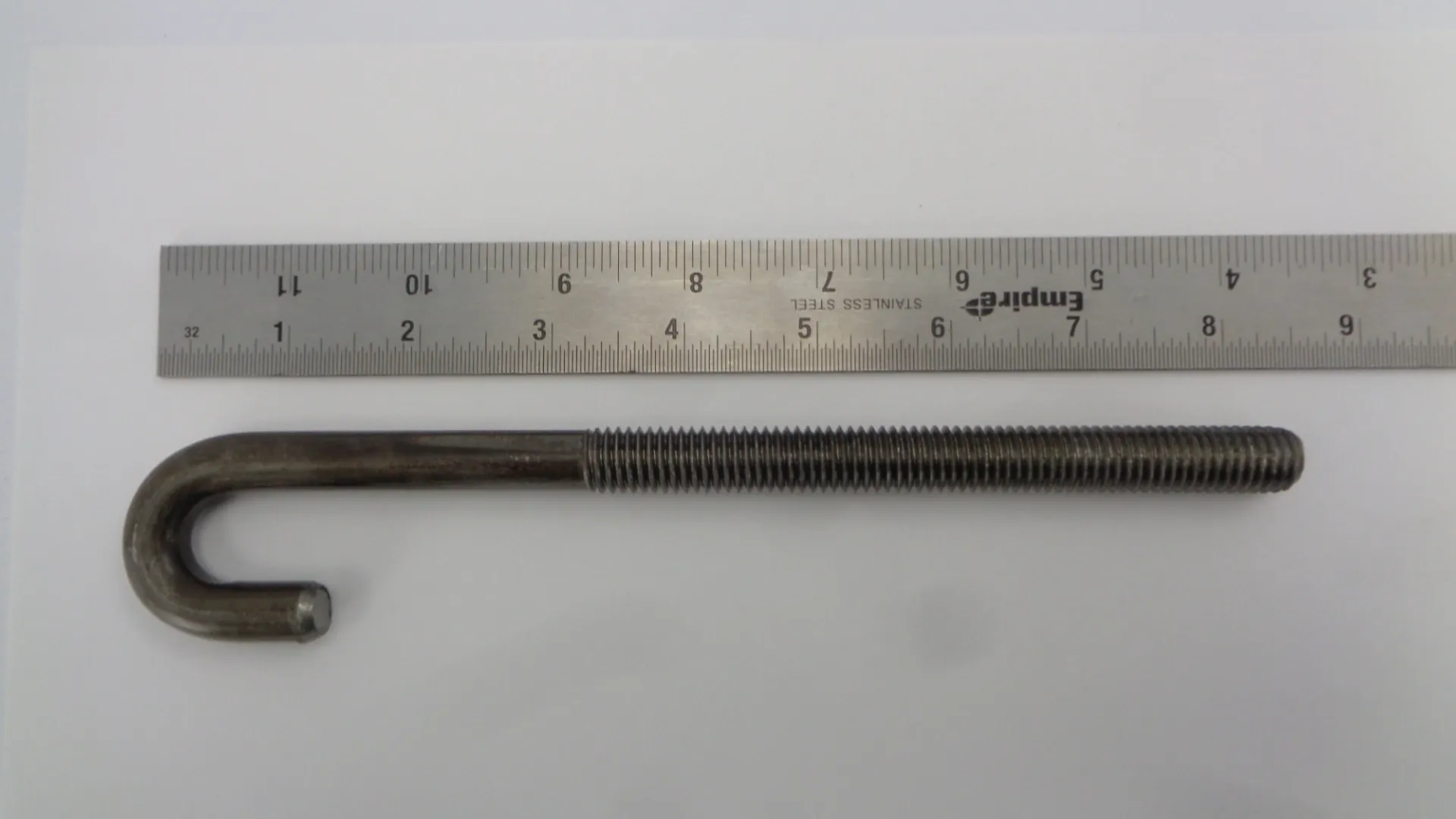 A metal screw rod placed next to a ruler for measurement.