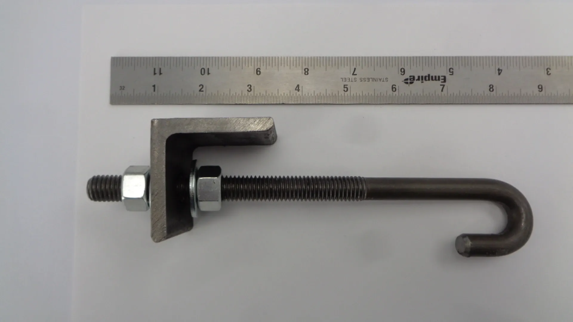 A metal clamp bolt with a nut and a ruler for scale.