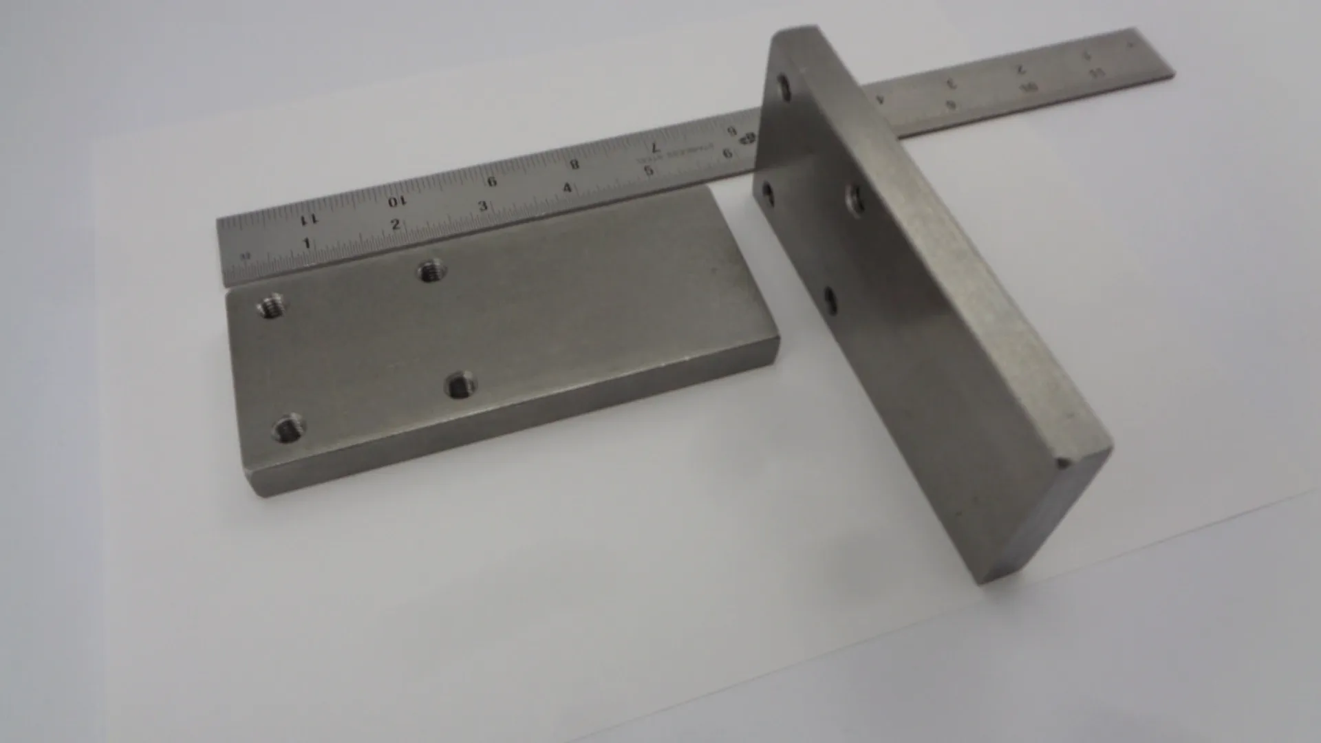 Two metal L-shaped brackets with holes on a white surface.