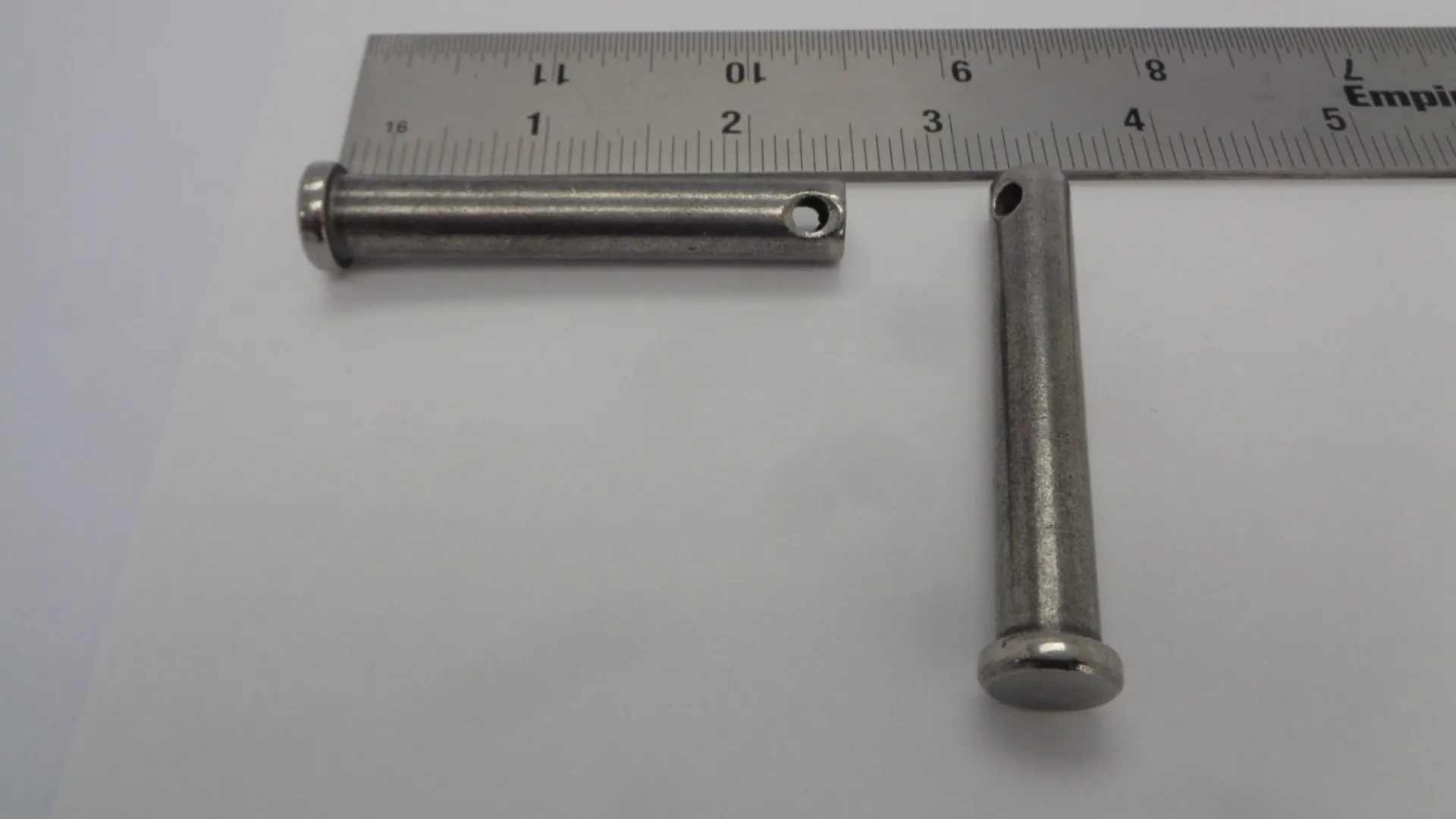 Two metal pins measured by a ruler, one with a hole.