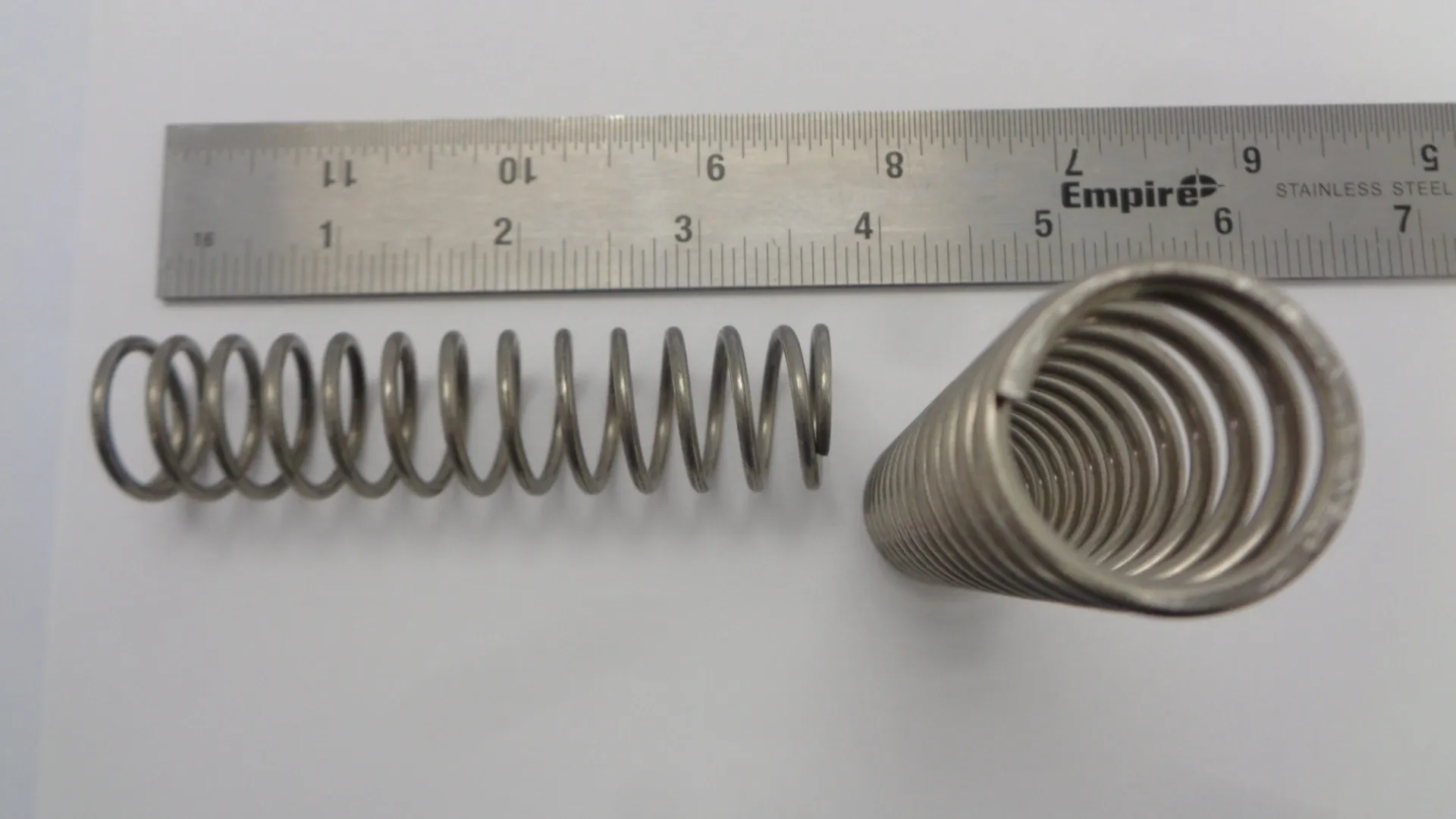 Metal compression spring with a ruler for scale.