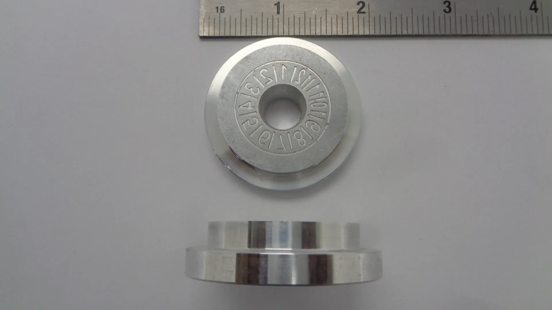 Two metallic circular parts with engraved text and a ruler for scale.
