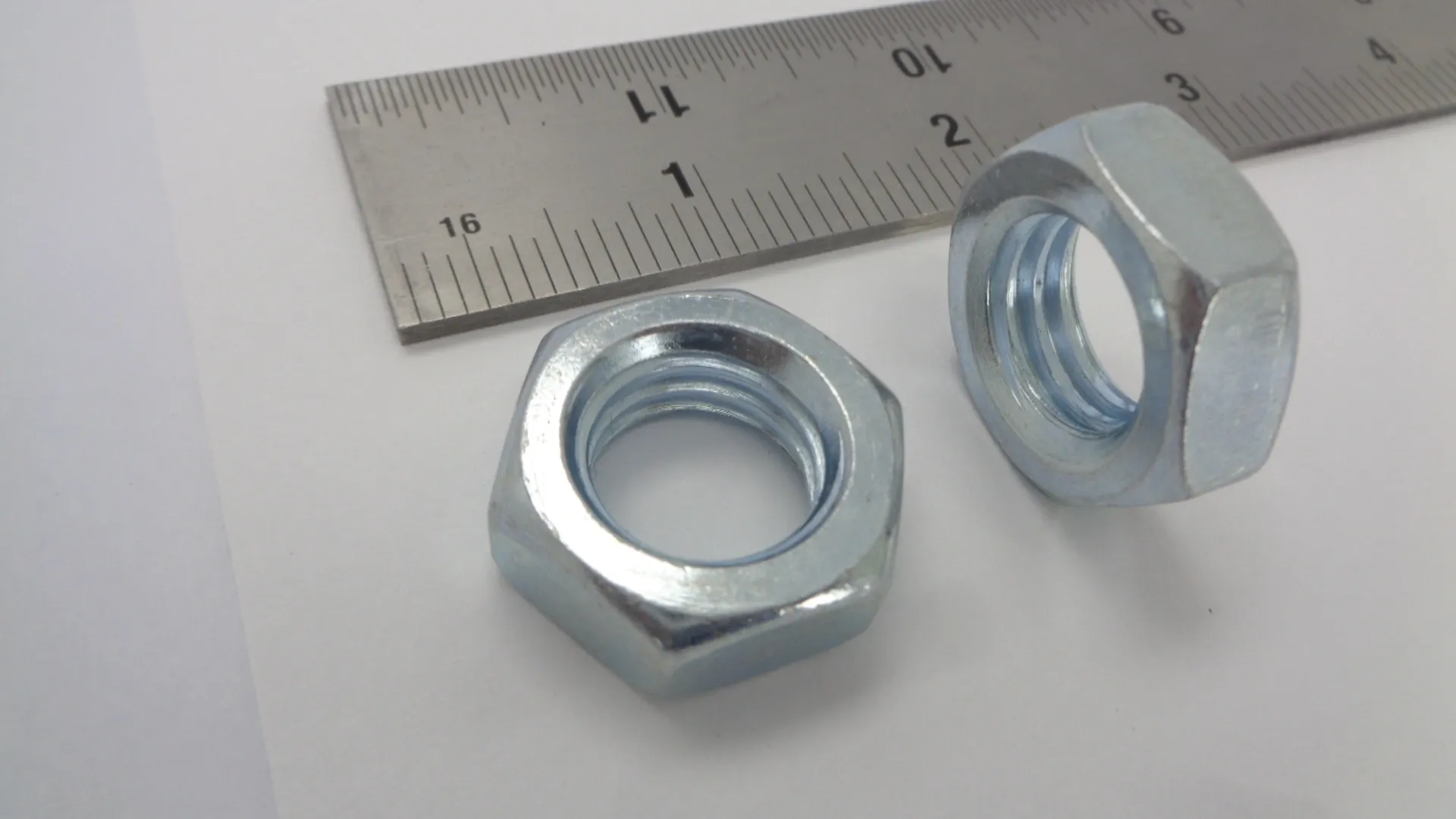 Two metal hex nuts beside a ruler for scale.