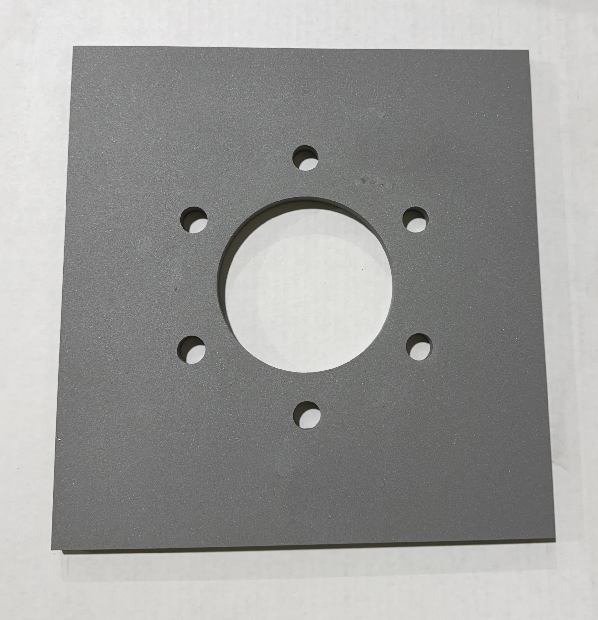 Square metal plate with a central large hole and six smaller surrounding holes.