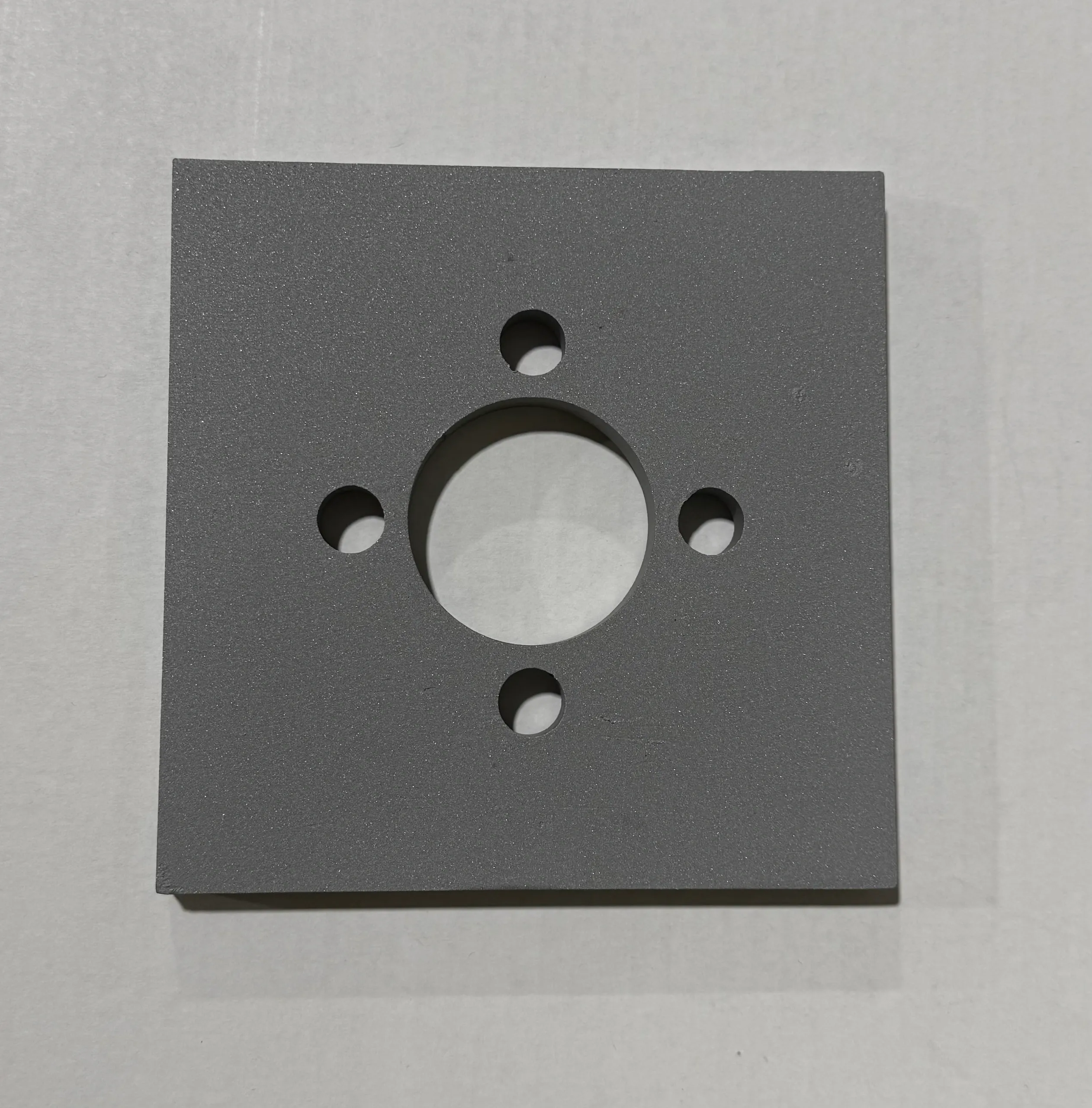 Square metal plate with multiple drilled holes.