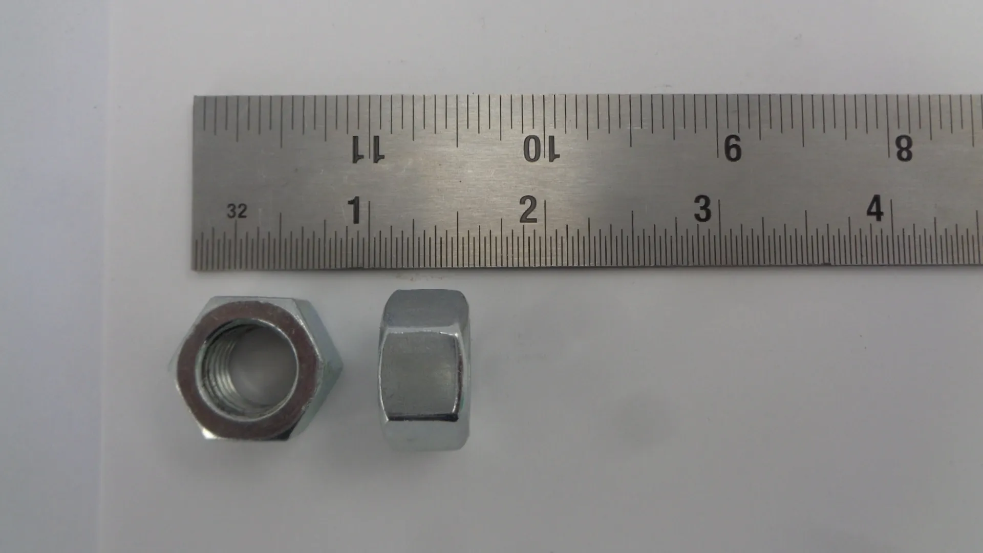 Two small metallic nuts placed near a ruler for size reference.