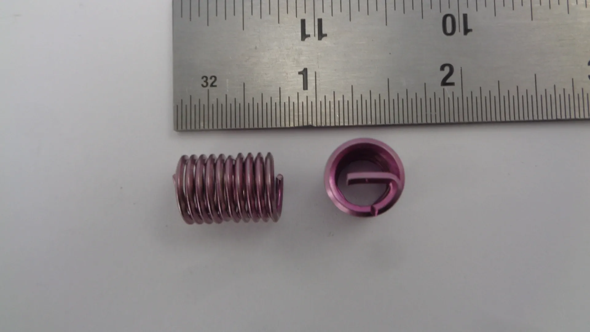 Small purple metal spring and its end cap next to a ruler.