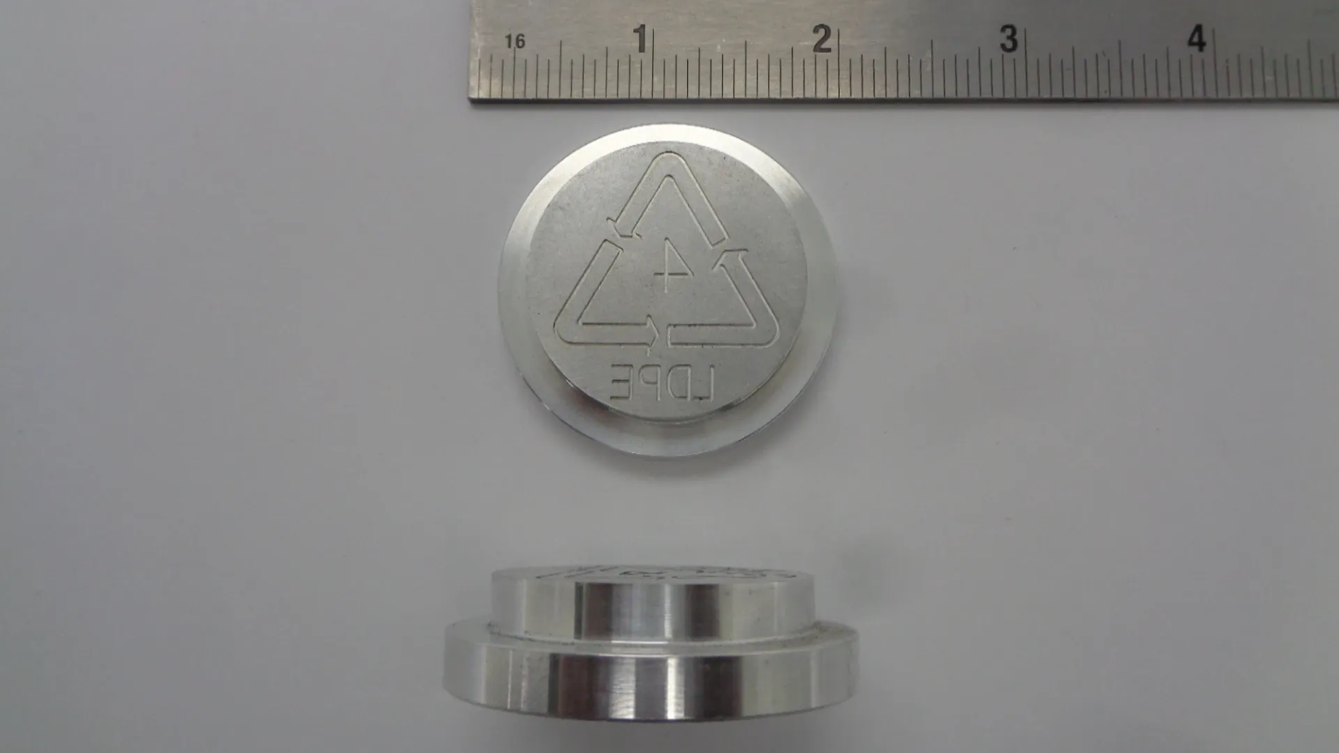 Metallic circular object with engraved symbols next to a ruler.